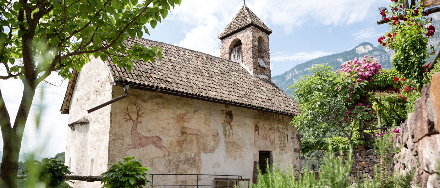 Hotels on Lago di Monticolo: South Tyrol awaits Old chapel with frescoes in a green garden and mountains in the background