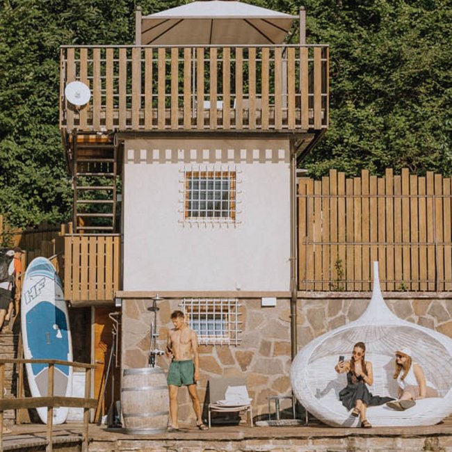 Hotel am Montiggler See: Gartenhotel Moser Menschen entspannen an einem See vor einem kleinen Haus mit Sonnenschirm