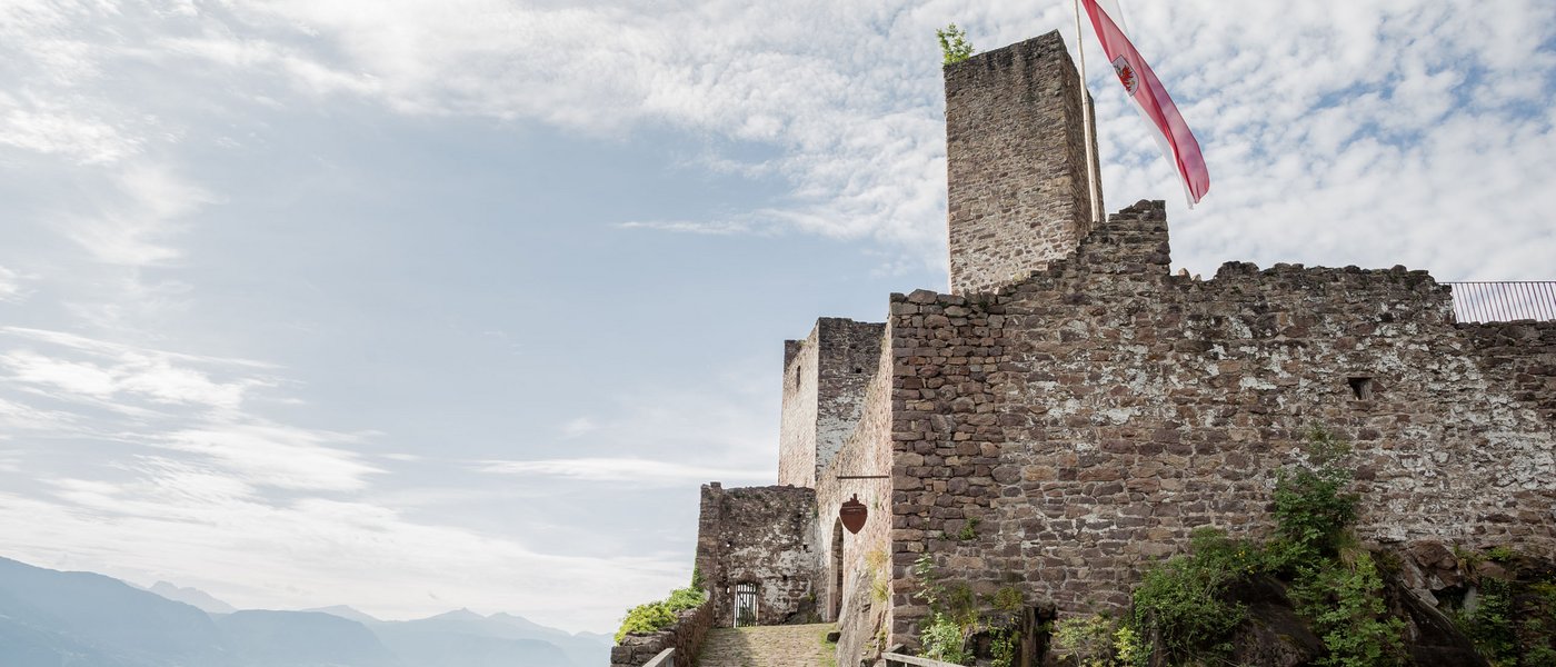 Hotels on Lago di Monticolo: South Tyrol awaits Wooden bridge leads to old stone castle with flag on a hill