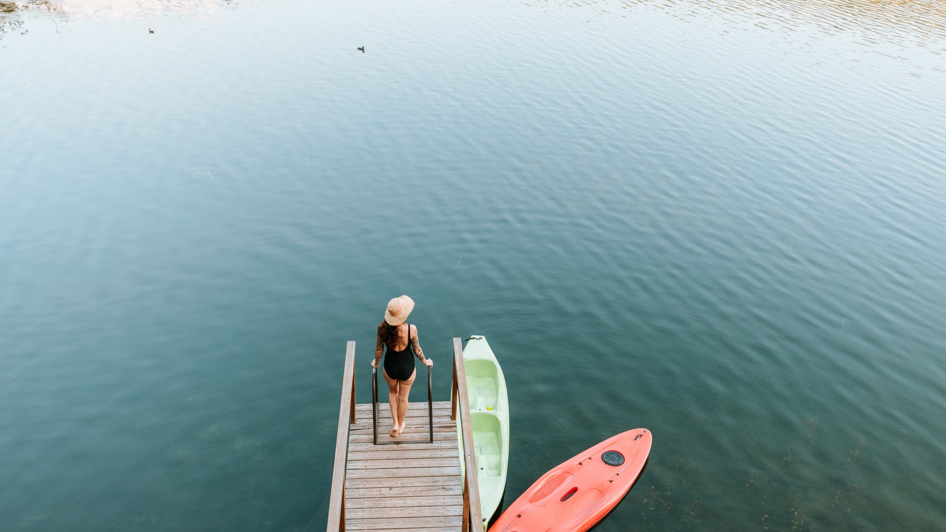 Hotels nahe dem Kalterer See 4-Sterne-Superior Frau in Badeanzug und Hut auf Steg über ruhigem Wasser neben Kajaks