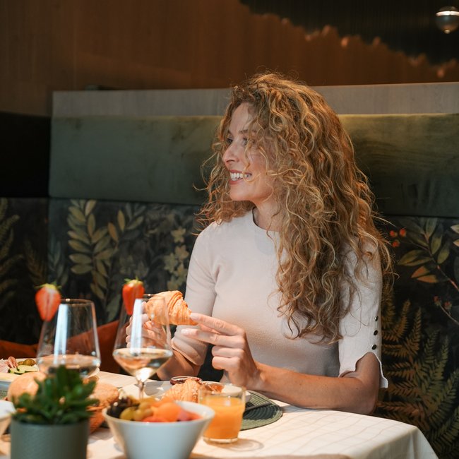 Day spa in South Tyrol: Gartenhotel Moser Woman with curly hair eating a croissant at breakfast in a restaurant