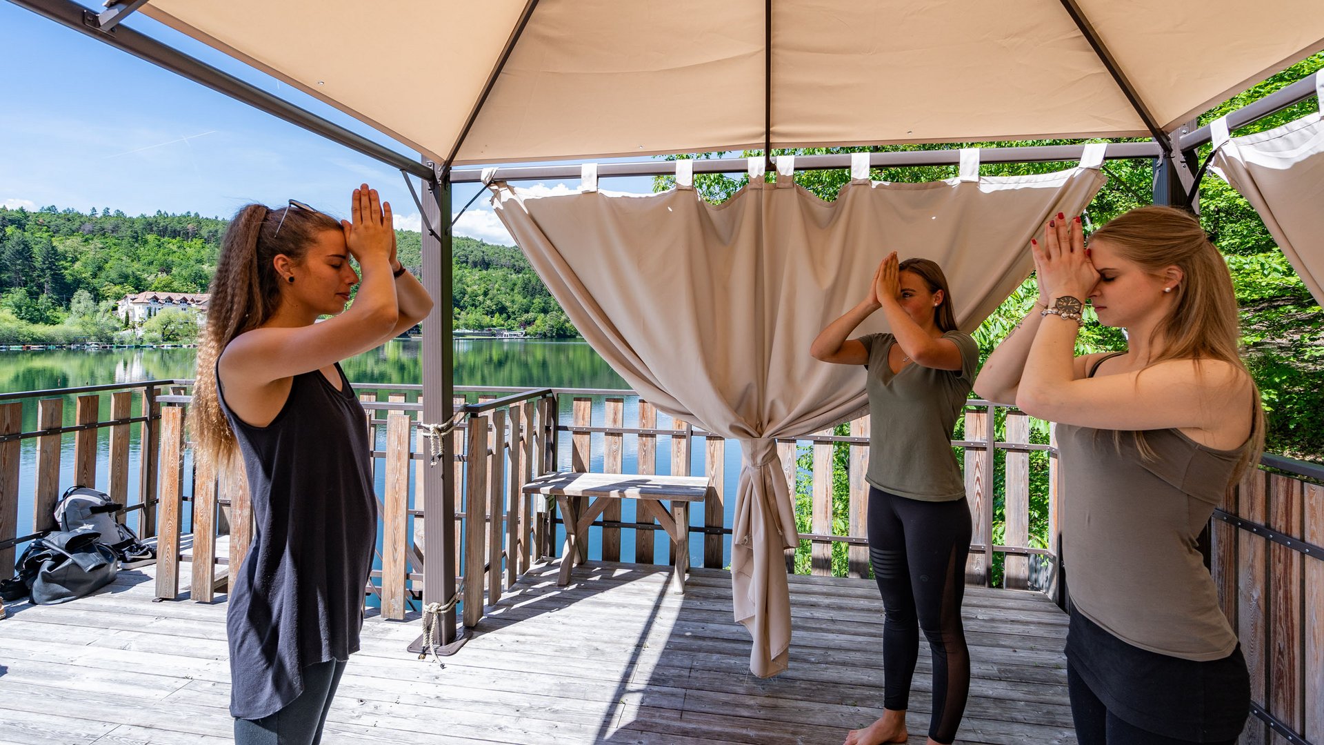 Hotel benessere in Alto Adige: posizioni Tre donne fanno yoga in piedi su una terrazza con vista sul lago