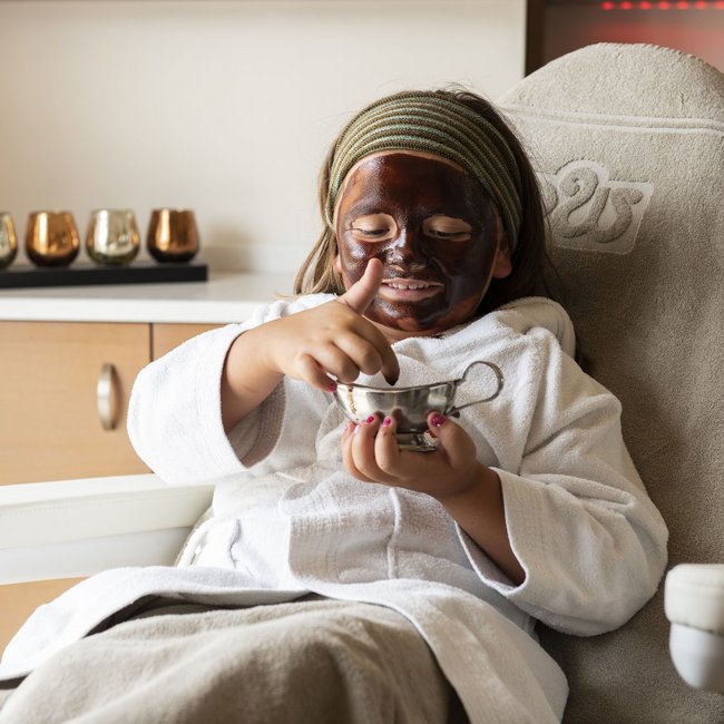 Familienhotel in Südtirol: Gartenhotel Moser Kind mit Gesichtsmaske sitzt entspannt im Wellnesssessel