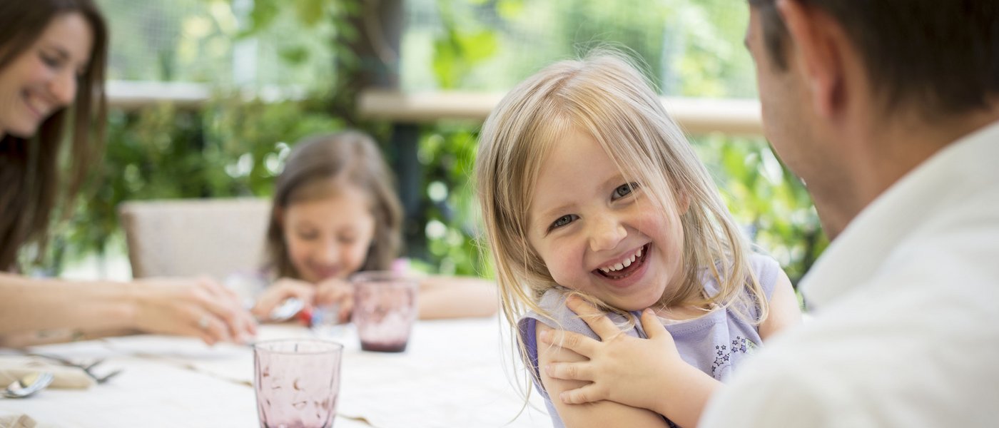 Kinderhotel am See: Gartenhotel Moser Lachendes Mädchen am Esstisch mit Familie im Garten
