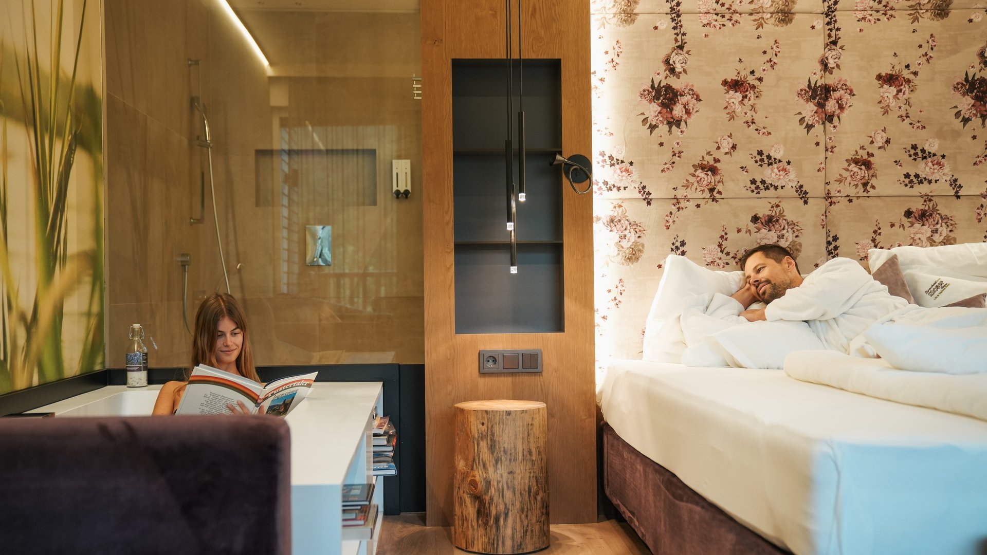 Hotel an der Weinstraße in Südtirol Frau liest Buch in Badewanne, Mann liegt auf dem Bett in einem gemütlichen Zimmer