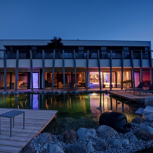 Day spa in South Tyrol: Gartenhotel Moser Modern house with illuminated pond and wooden terraces at night