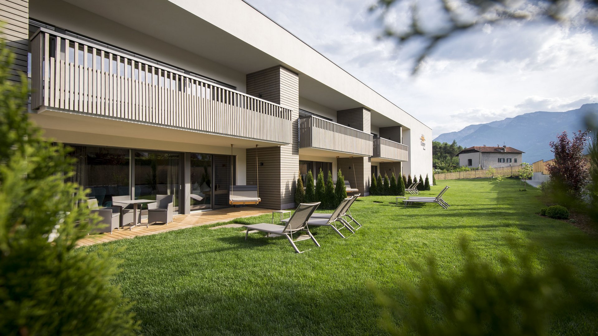 Hotel an der Weinstraße in Südtirol Moderner Gebäudekomplex mit Balkon und Liegestühlen auf großem Rasen