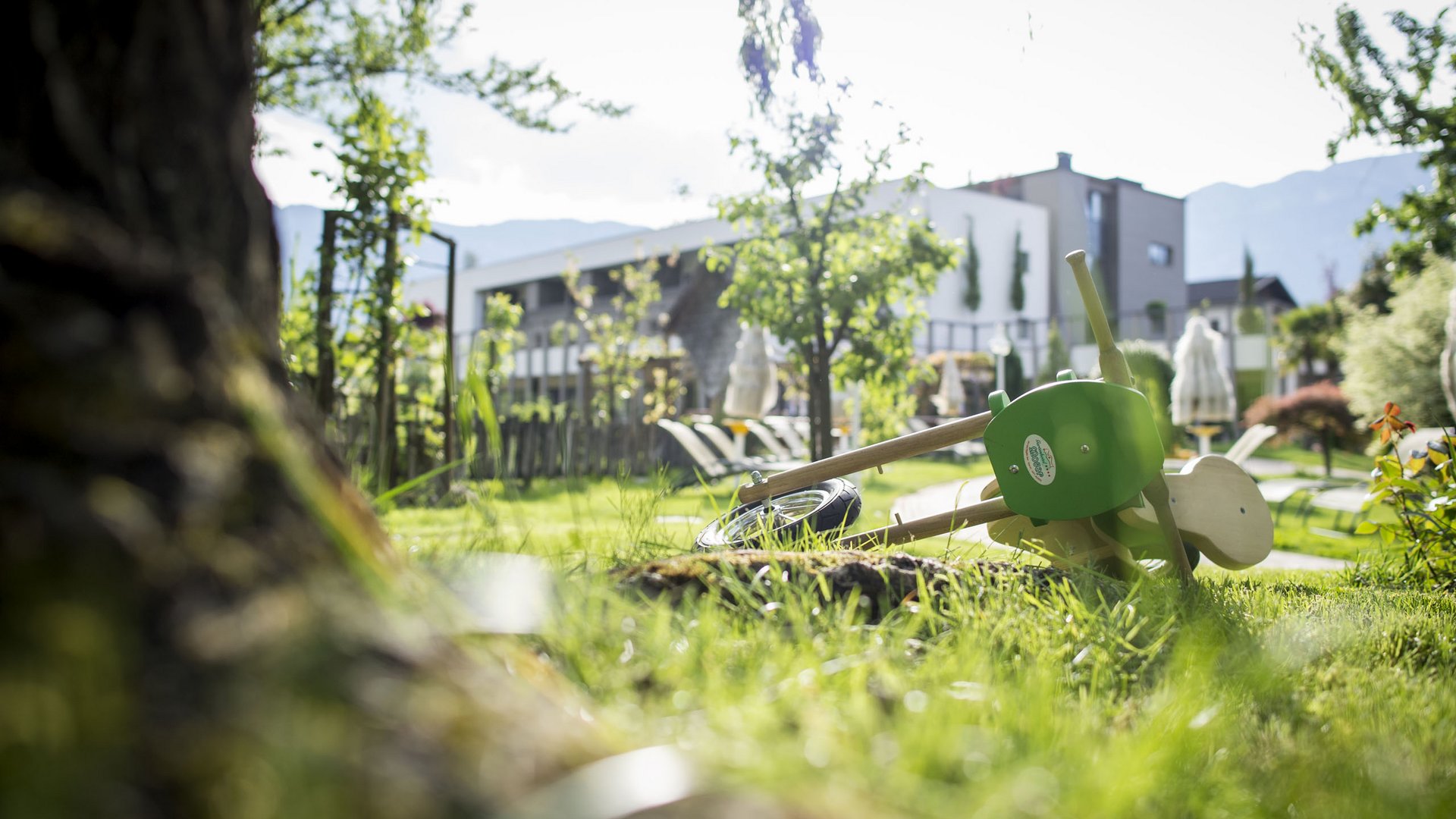 Familienhotel in Südtirol: Gartenhotel Moser Kinderspielzeug im Gras neben einem Baum in einem Garten vor einem modernen Gebäude