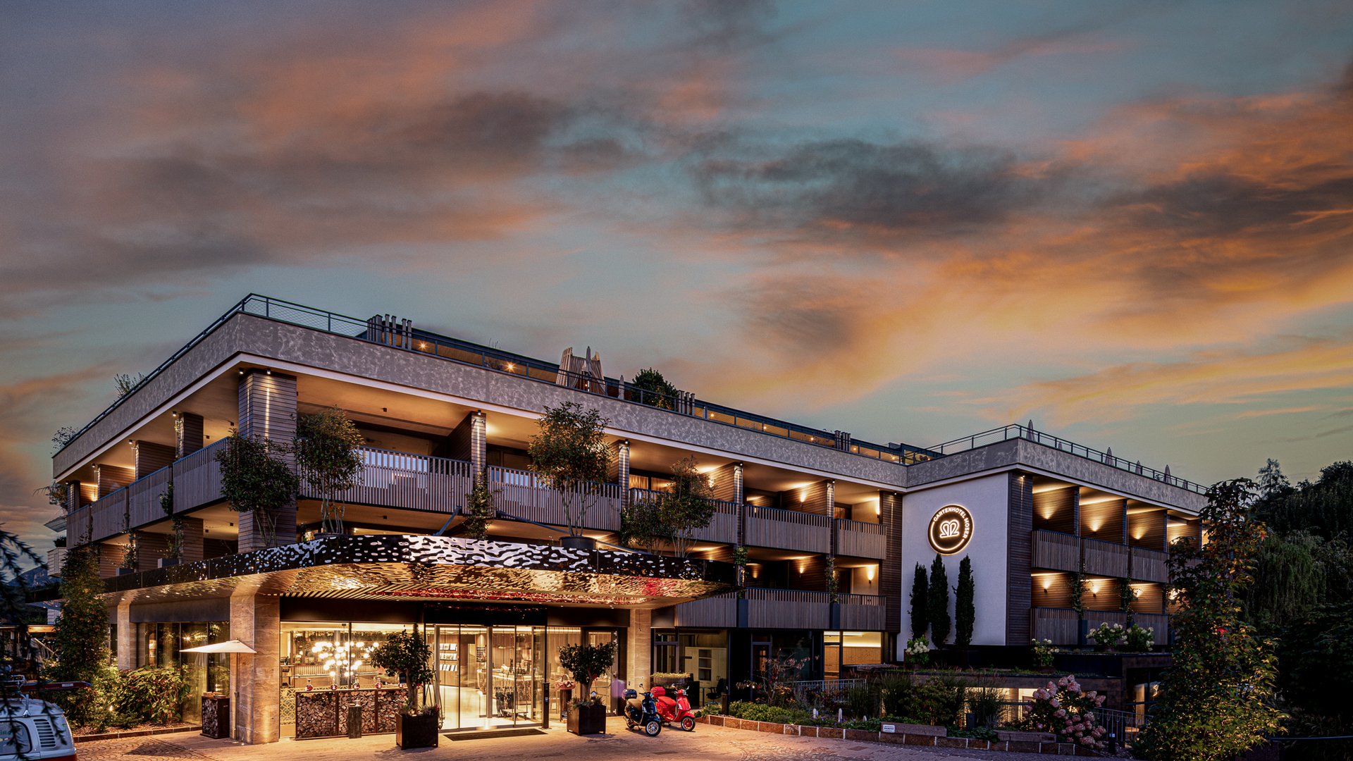 Hotels near Lago di Caldaro with 4-star superior service Modern hotel building at sunset with lit entrance and logo