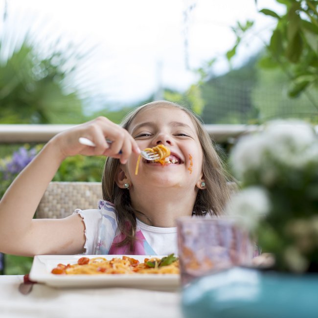Im Wellnesshotel glutenfrei genießen Mädchen isst lachend Spaghetti im Freien