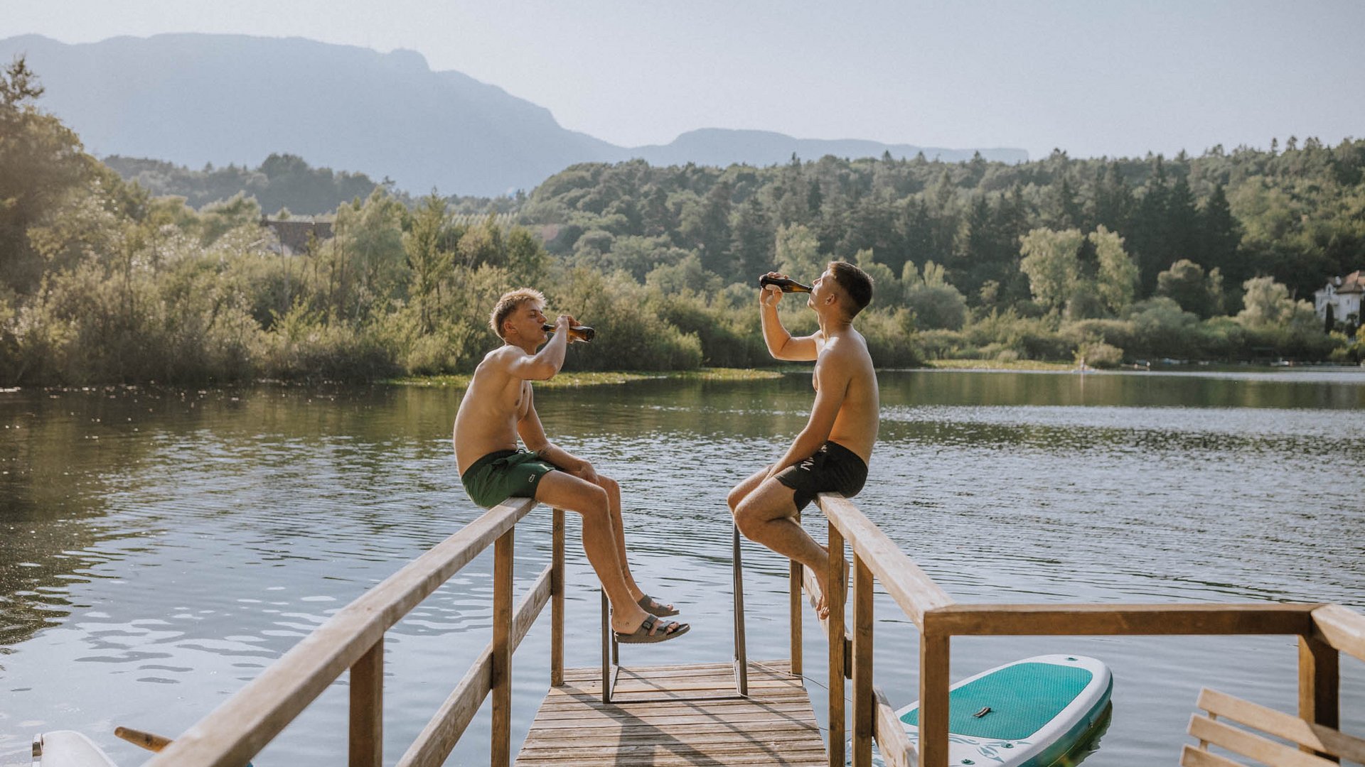 Wellnessurlaub am See: Gartenhotel Moser Zwei junge Männer sitzen auf Steg am See und trinken Bier im Freien