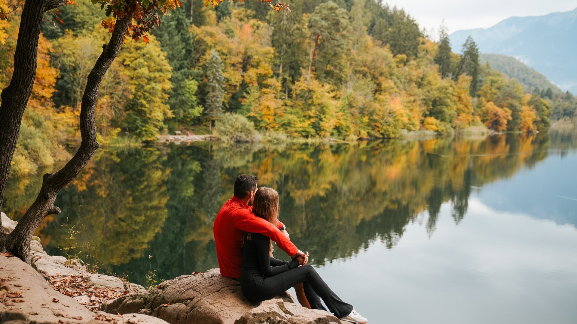 Hotels near Lago di Caldaro with 4-star superior service A couple sitting by a calm lake in an autumn forest