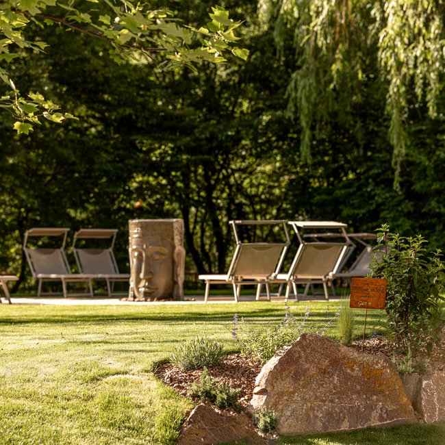 Neu ab 2026 im Gartenhotel Moser Sonnige Liegestühle im Garten mit grünen Bäumen und einer Steinskulptur