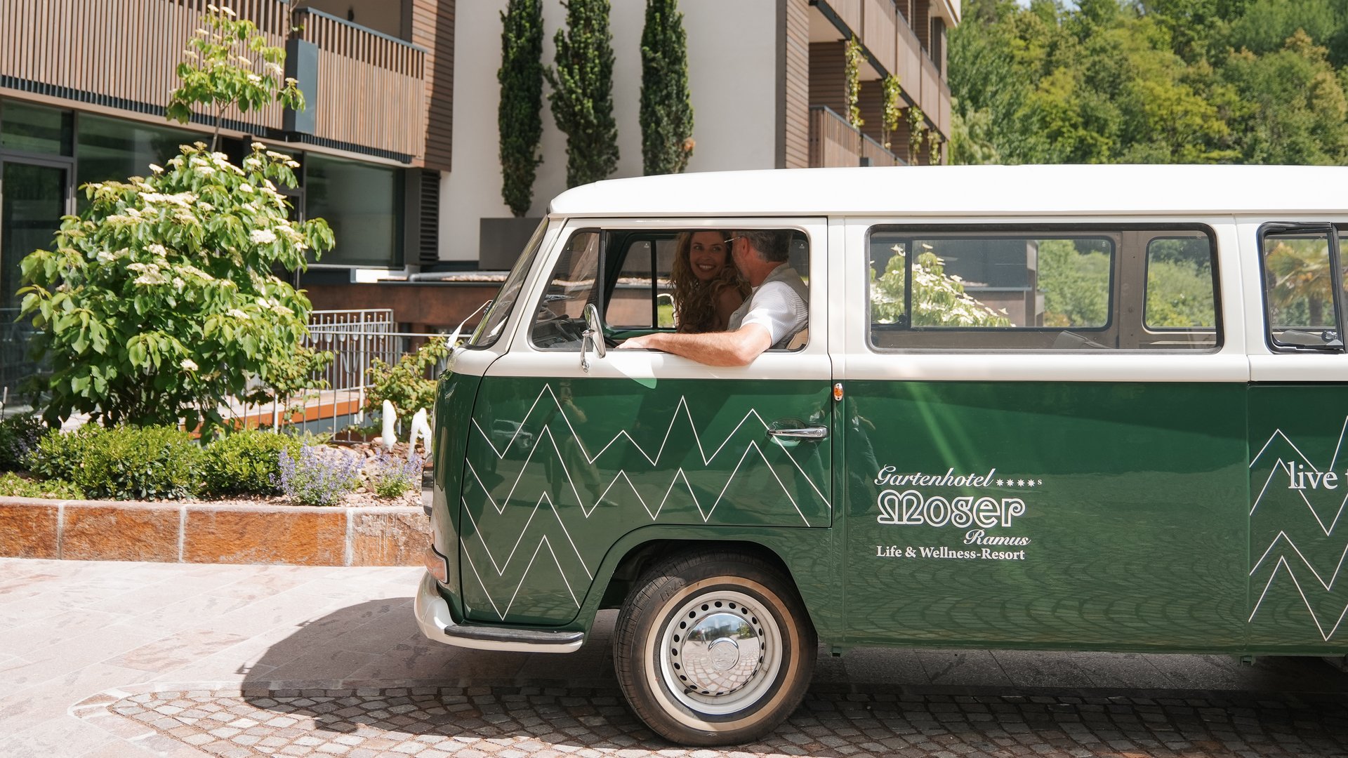 Hotels in Eppan, Südtirol: Anfahrt Grüner Van vor dem Gartenhotel Moser mit Paar im Inneren