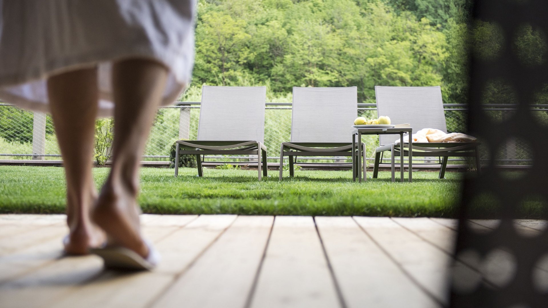 Hotel wellness in Alto Adige per soli adulti Donna in accappatoio cammina verso tre lettini sulla terrazza con prato verde