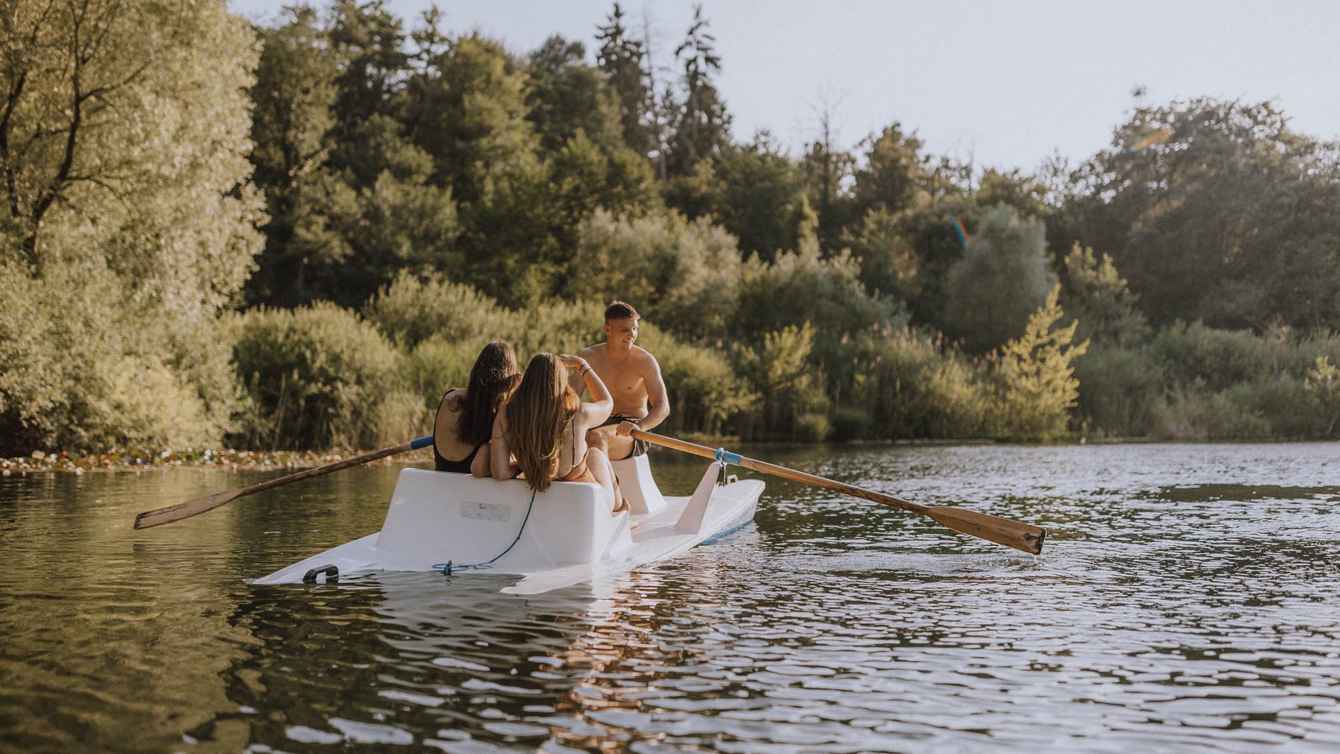Hotel am Montiggler See: Gartenhotel Moser Drei Personen rudern auf einem See umgeben von Bäumen an einem sonnigen Tag