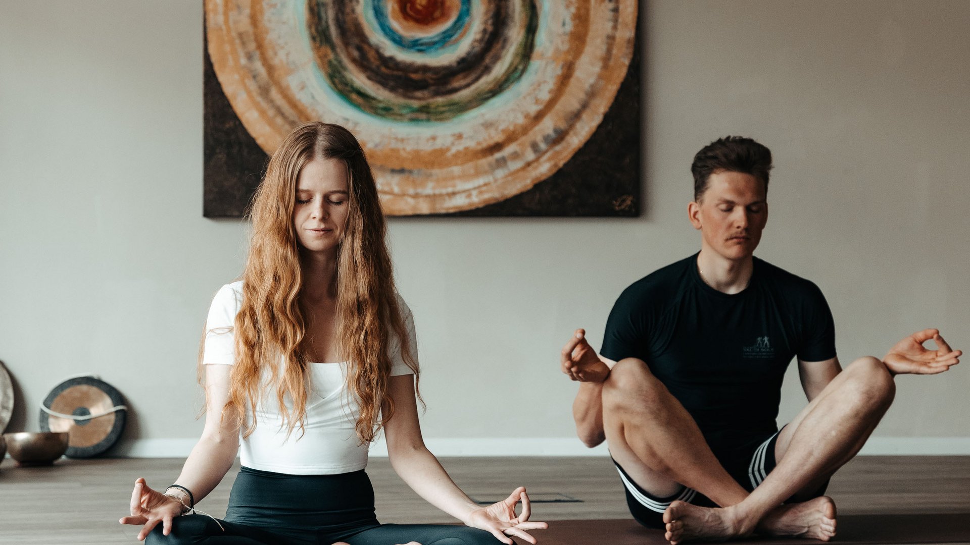 Yoga in Alto Adige Coppia pratica meditazione seduta su tappetini yoga davanti a un quadro astratto