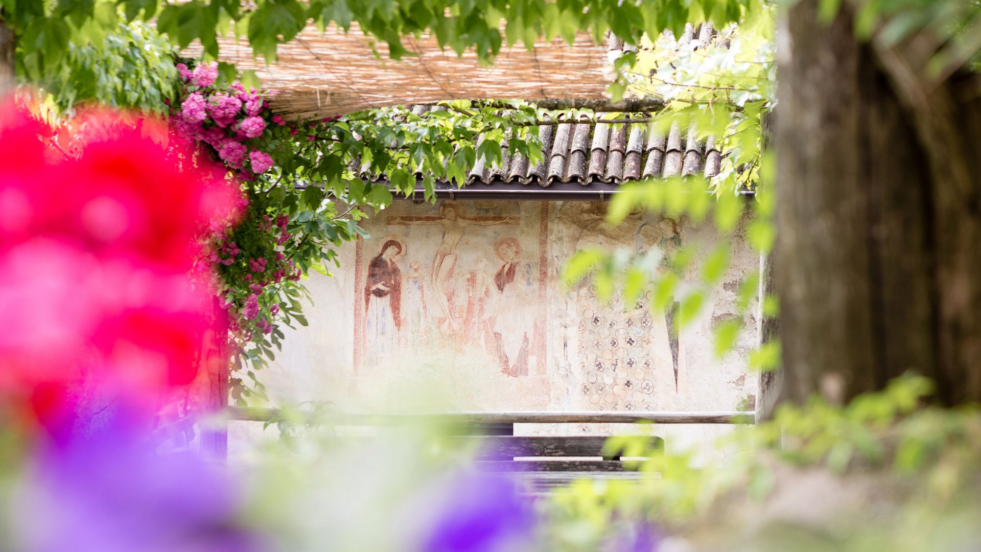 Kalterer See – Hotel in der Nähe Blick auf antikes Wandgemälde durch bunte Blumen und grünes Laub