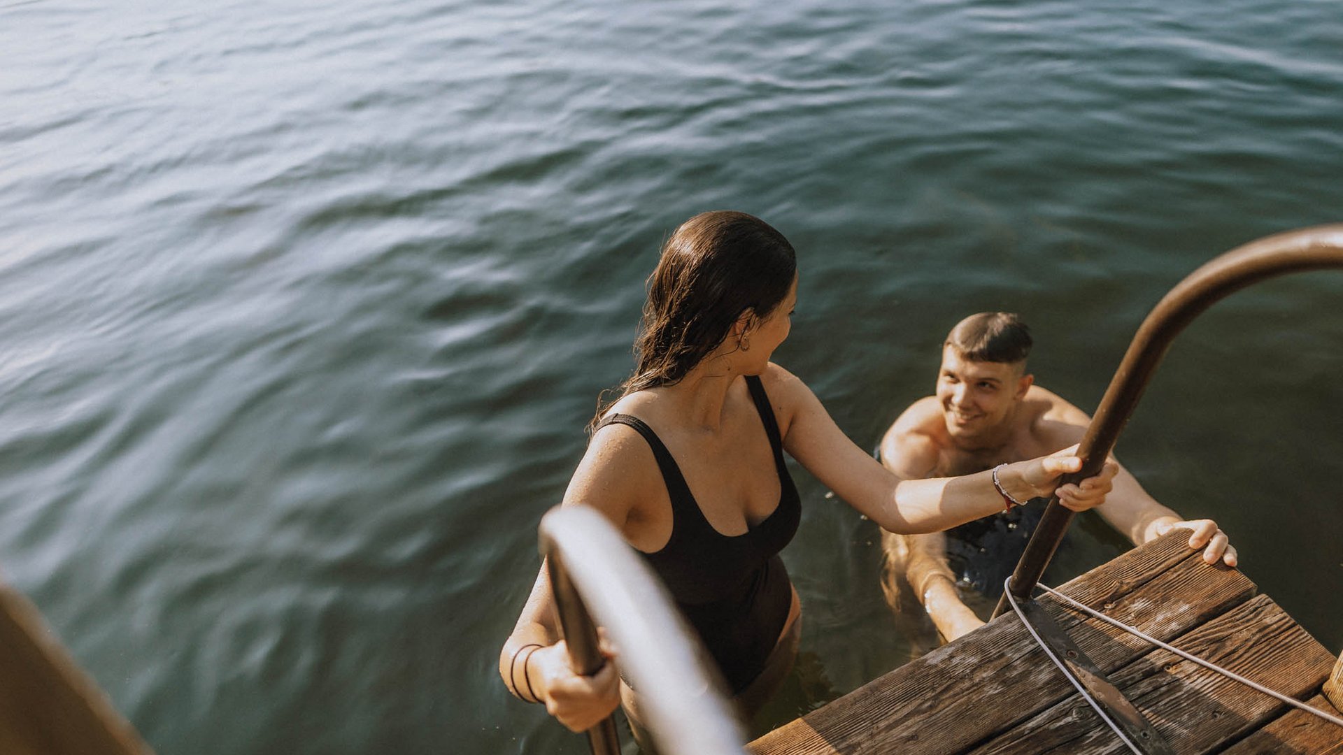 Laghi balneabili in Alto Adige: cosa c’è da sapere Donna sale da una scala dall'acqua, uomo la guarda dall'acqua