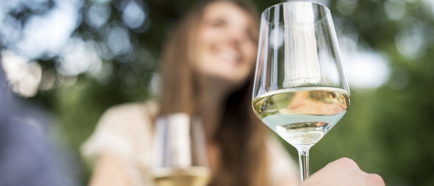 Hotel on the Wine Road in South Tyrol Close-up of white wine glass with smiling woman blurred in the background