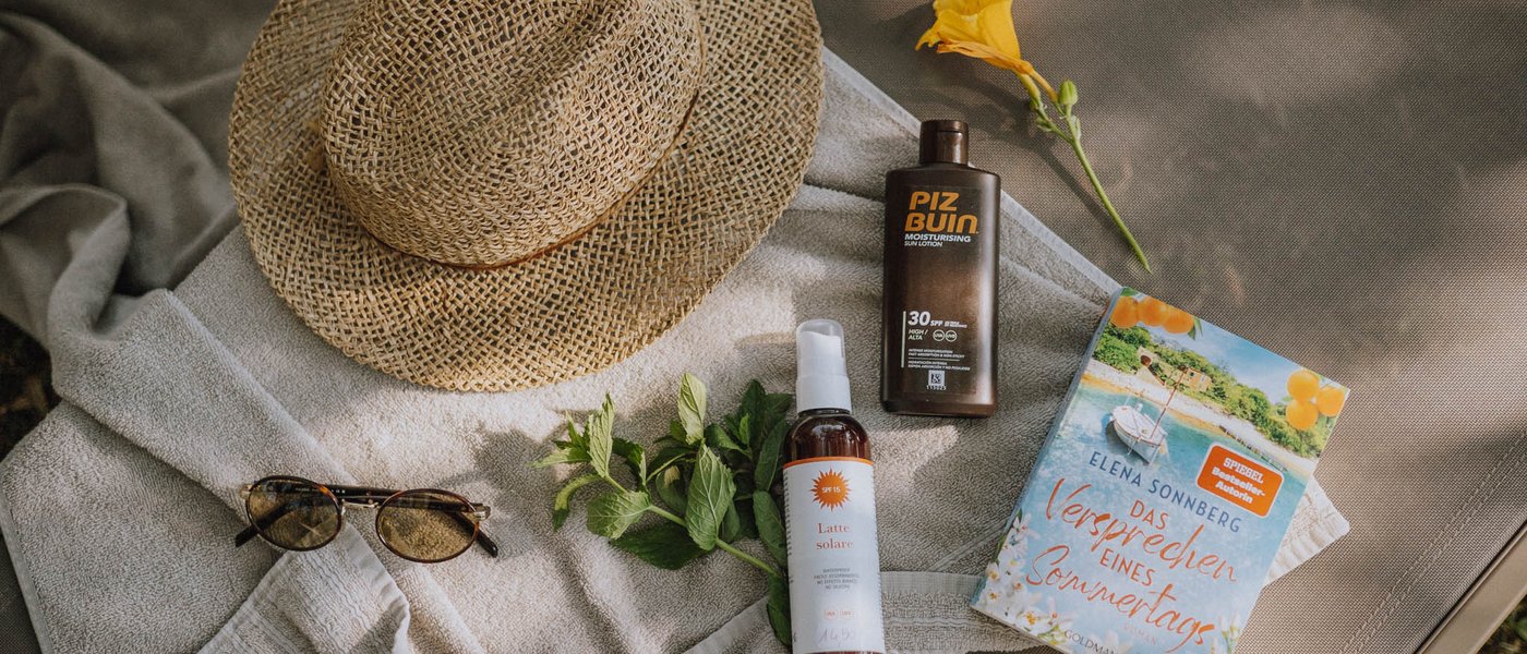 Laghi balneabili in Alto Adige: cosa c’è da sapere Oggetti estivi: cappello di paglia, creme solari, occhiali da sole, libro e fiore giallo
