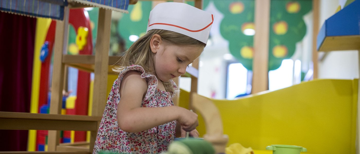 Familienhotel in Südtirol: Gartenhotel Moser Mädchen spielt in einer Kinderküche mit Kochmütze und Spielutensilien