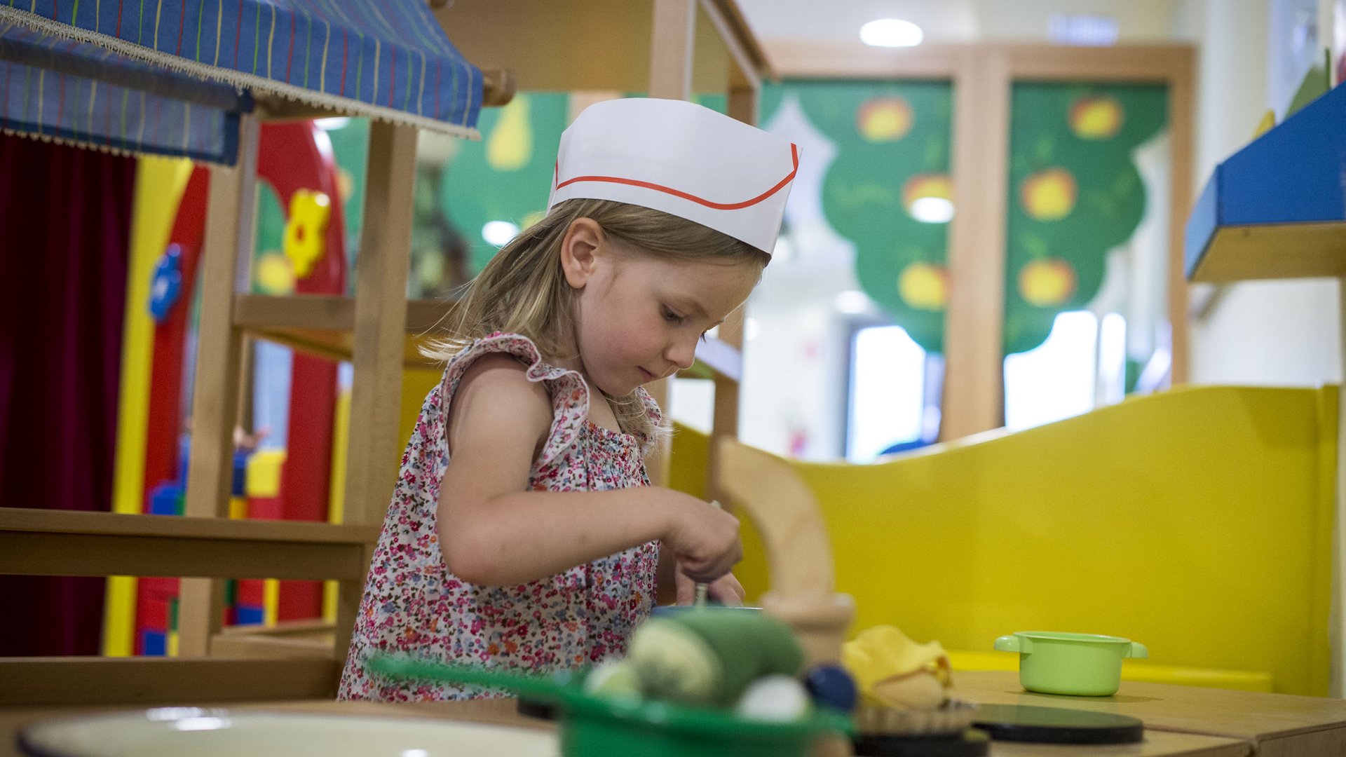 Children’s hotels in South Tyrol with 4-star-S service Girl playing in a toy kitchen wearing a chef hat with play utensils