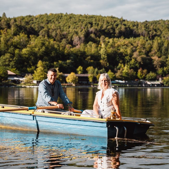 Hotels bei Eppan: Gartenhotel Moser Zwei Menschen in einem blauen Ruderboot auf einem See mit Wald im Hintergrund