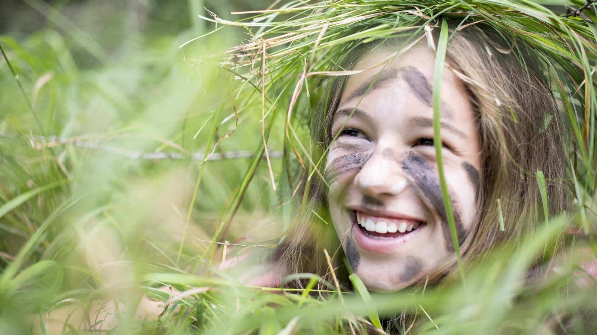 Children’s hotels in South Tyrol with 4-star-S service Smiling girl with camouflage face paint and grass wreath outdoors