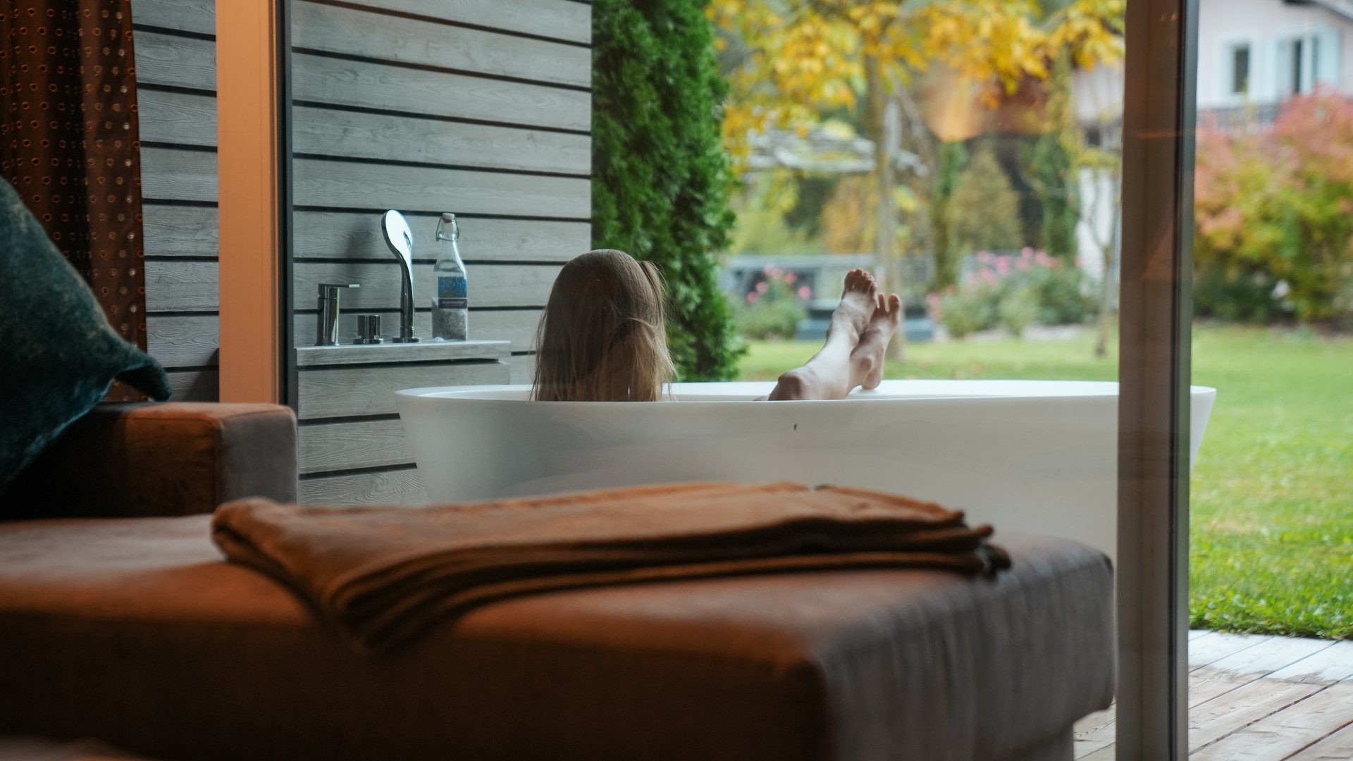 Hotel an der Weinstraße in Südtirol Person entspannt in einer Badewanne mit Blick auf Garten im Herbst