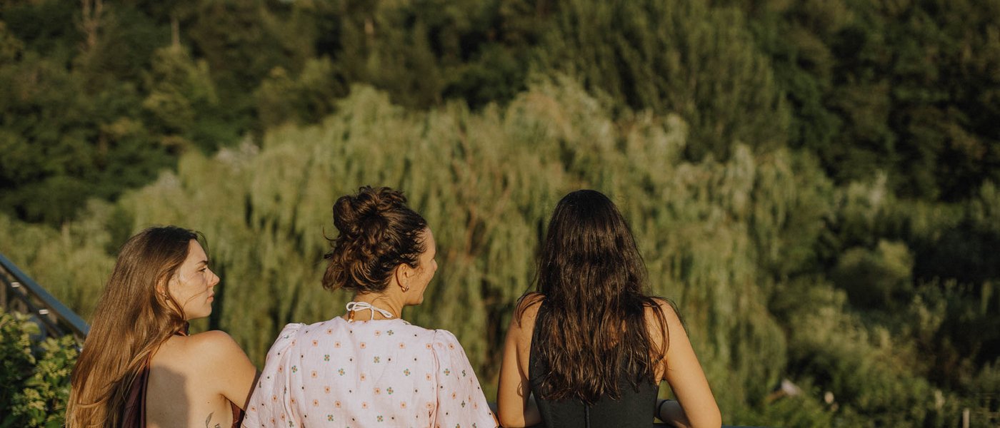 Hotel bei Eppan an der Weinstraße: Gartenhotel Moser Drei Frauen blicken von einem Balkon aus auf einen bewachsenen Wald