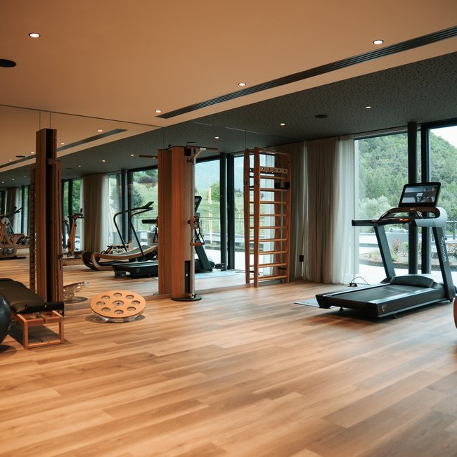 Sporthotels in Südtirol: Gartenhotel Moser Moderner Fitnessraum mit Holzfußboden und großen Fenstern mit Bergblick