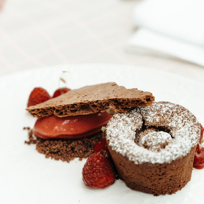 Wellness hotel with gourmet cuisine: Gartenhotel Moser Chocolate dessert with powdered sugar, raspberries, and crispy layer on white plate
