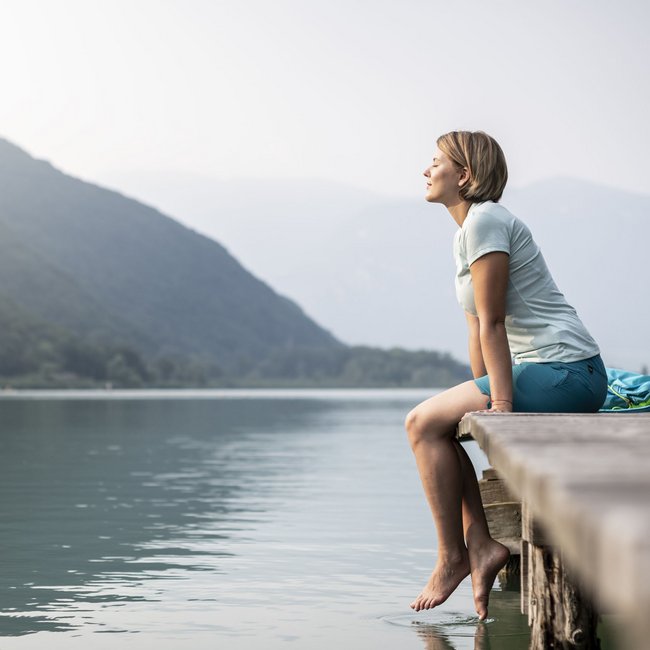 Hotel am Montiggler See: Gartenhotel Moser Frau sitzt entspannt am Steg und genießt die Aussicht auf den See und die Berge