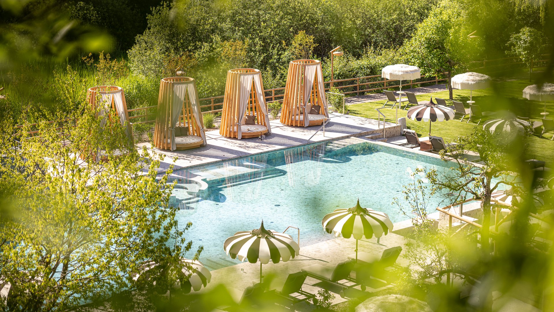 Hotel in Alto Adige con piscina Piscina all'aperto con lettini, ombrelloni e letti di legno in un ambiente verde
