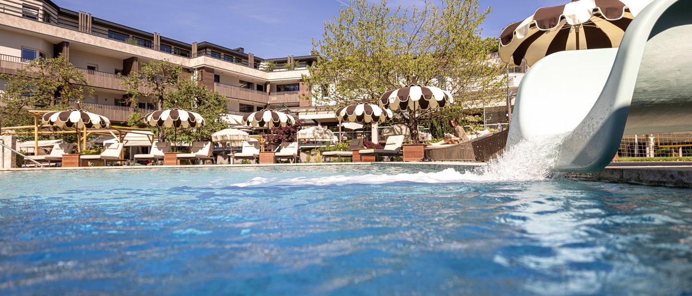 Hotel in Alto Adige con piscina Piscina all'aperto con scivolo d'acqua e ombrelloni davanti all'hotel