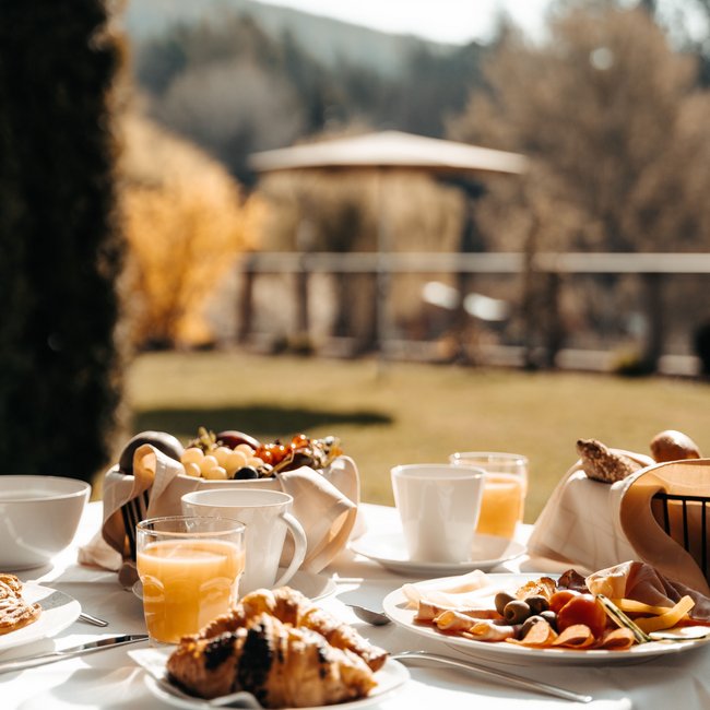 Day spa in South Tyrol: Gartenhotel Moser Breakfast table with croissants, juice, and fruit in sunny garden setting