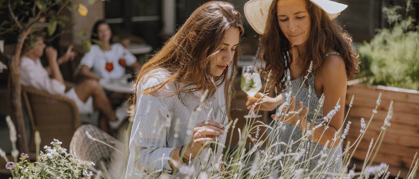 Hotels nahe dem Kalterer See 4-Sterne-Superior Zwei Frauen betrachten Pflanzen in einem Garten bei schönem Wetter