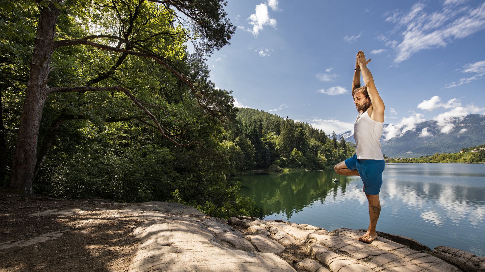 Yoga in Alto Adige Uomo pratica yoga sul lago circondato da boschi e montagne