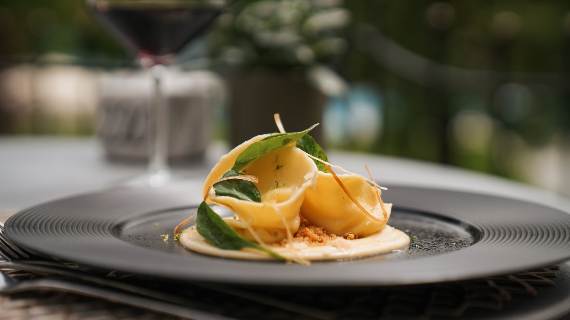 Hotel bei Eppan an der Weinstraße: Gartenhotel Moser Fein angerichtete Pasta mit grünen Blättern auf einem schwarzen Teller