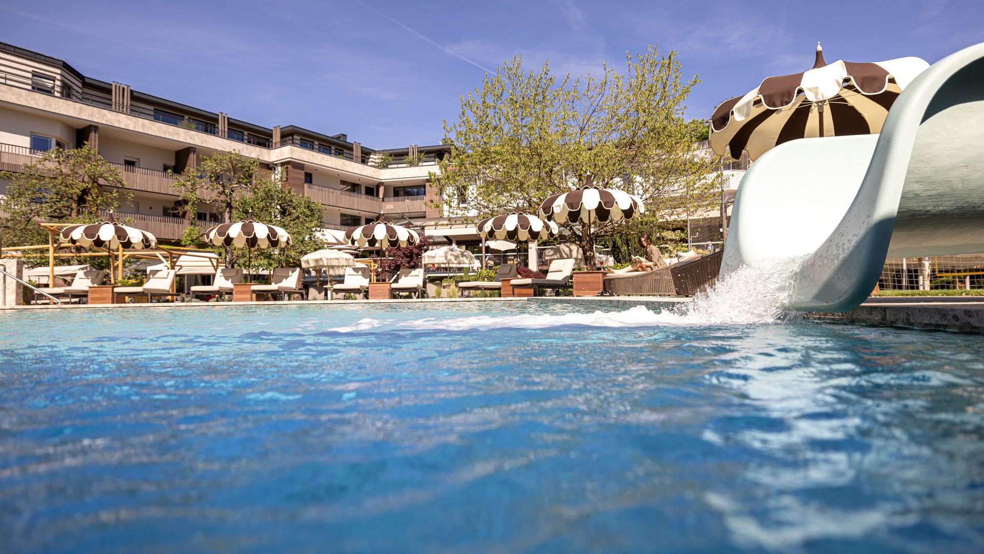 Piscina all'aperto con scivolo d'acqua e ombrelloni davanti all'hotel