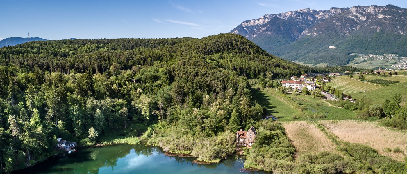 Lago di Caldaro: passeggiata e varie attività nei dintorni del Gartenhotel Moser Lago con foresta, casa e montagne sotto cielo blu