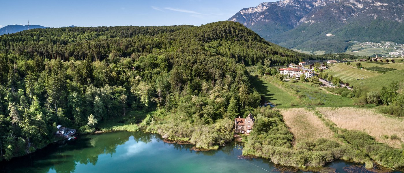 Laghi balneabili in Alto Adige: cosa c’è da sapere Lago con foresta, casa e montagne sotto cielo blu