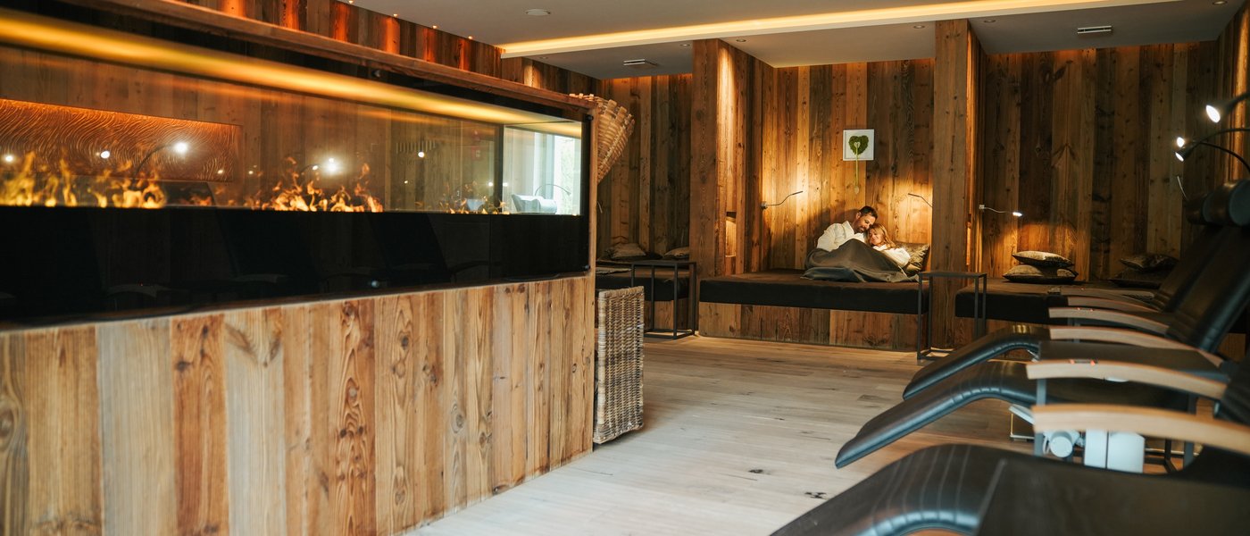 Wellnesshotel mit Whirlpool und Saunawelt Gemütlicher Ruheraum mit Holzvertäfelung, Ofenfeuer und entspannenden Liegestühlen