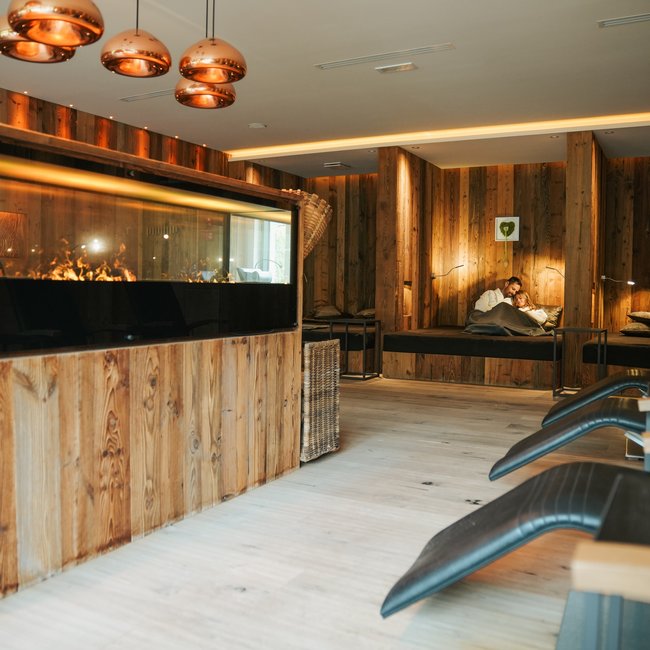 Day spa ad Appiano, al Gartenhotel Moser Sala relax accogliente con pannelli in legno, camino acceso e lettini confortevoli