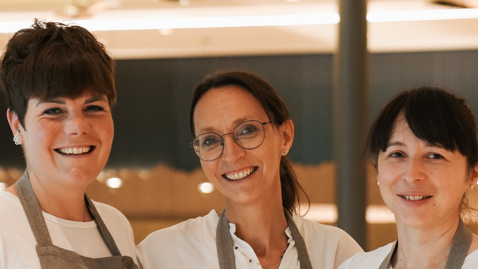 4-Sterne-S-Hotels in Südtirol: Jobs Drei lächelnde Kellnerinnen in grauen Schürzen in einem Restaurant