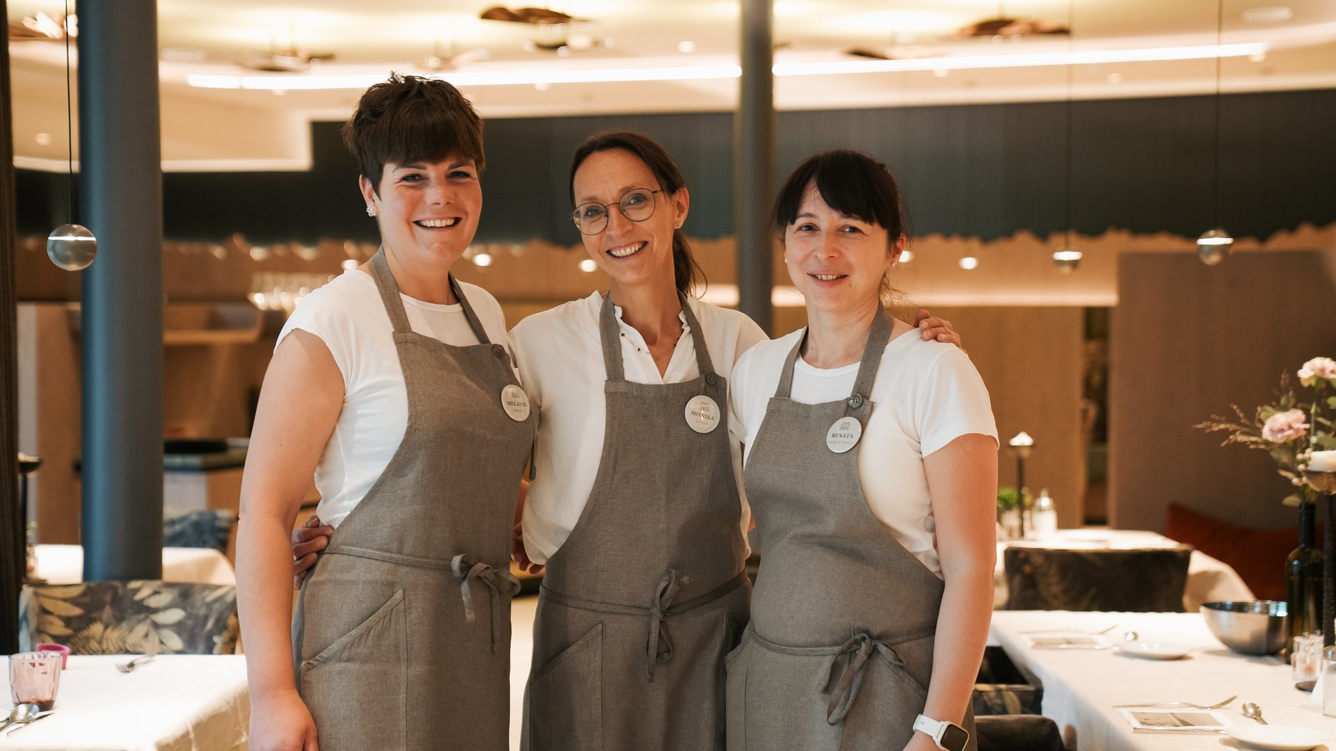 Hotels bei Eppan: Gartenhotel Moser Drei lächelnde Kellnerinnen in grauen Schürzen in einem Restaurant