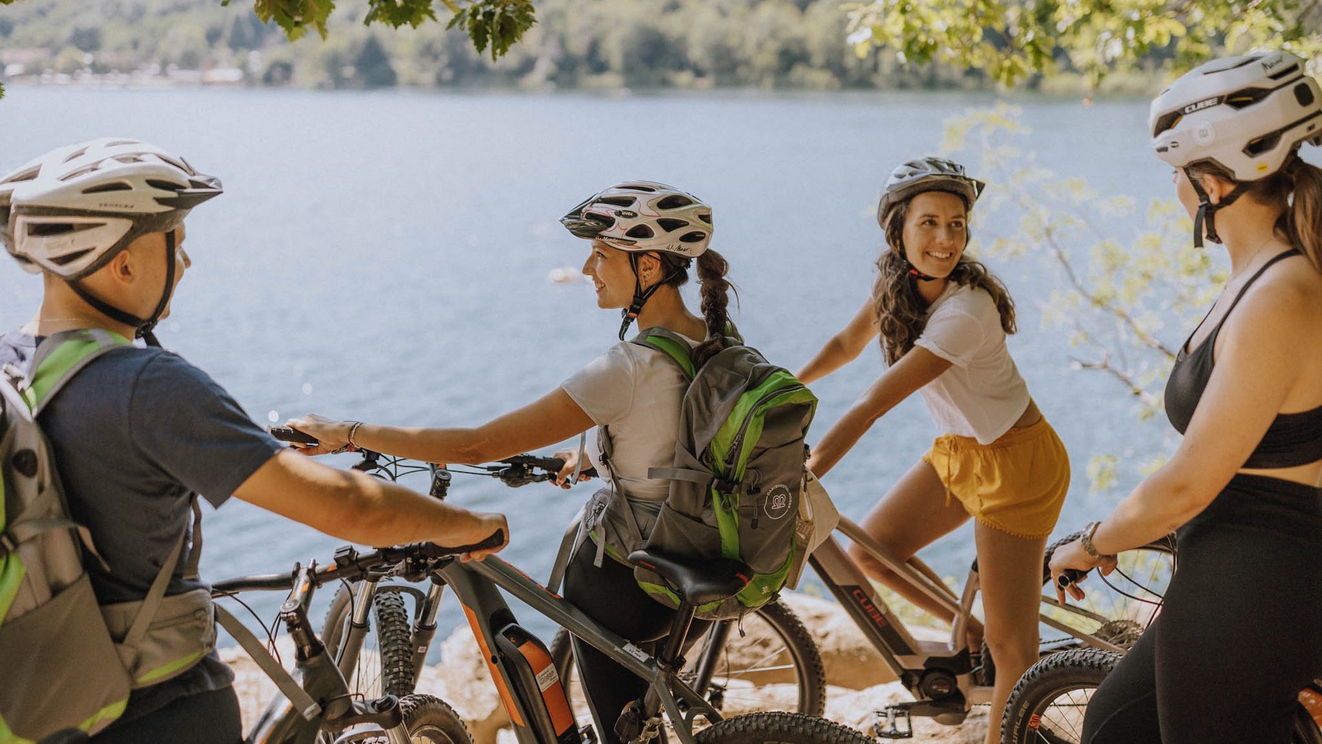 Gruppo di ciclisti con caschi vicino a un lago circondato da alberi