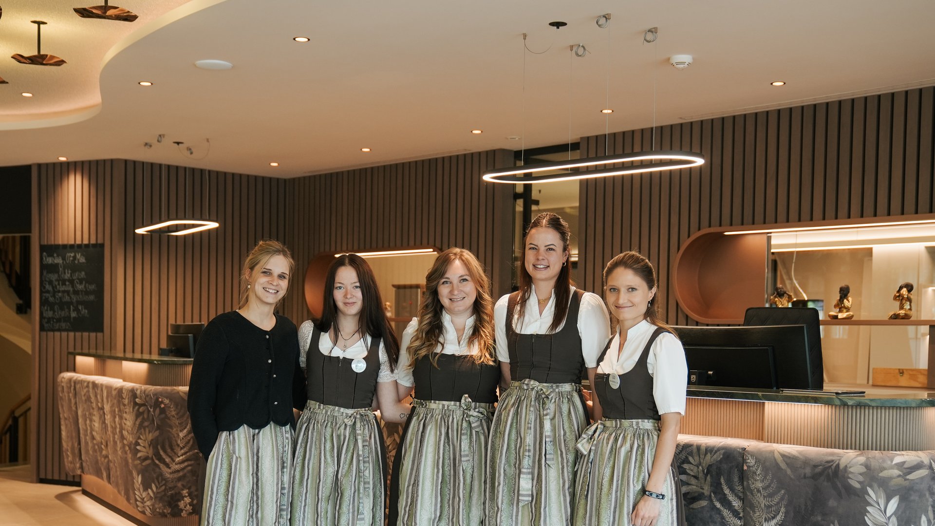 4-Sterne-S-Hotels in Südtirol: Jobs Fünf Frauen in traditionellen Dirndlkleidern stehen in modernem Empfangsbereich