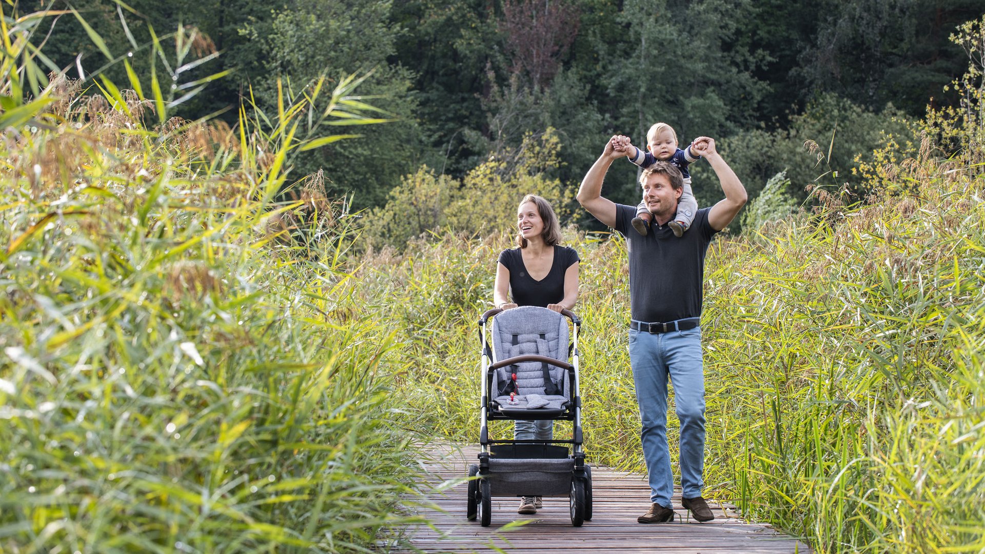 Kinderhotel am See: Gartenhotel Moser Familie mit Baby spaziert auf Holzsteg durch grüne Natur